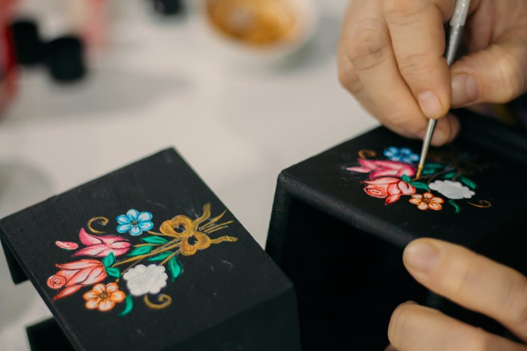 Close-up of an artisan hand-painting a floral design on a black decorative box.
