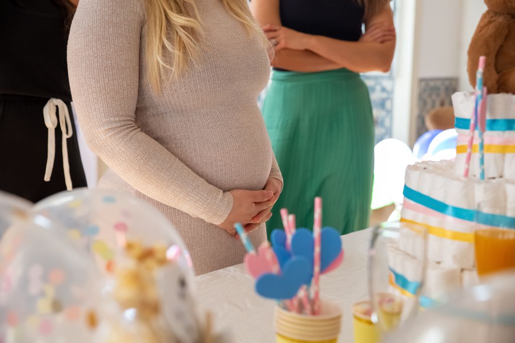 A joyful baby shower event featuring a pregnant woman surrounded by festive decorations and a diaper cake.