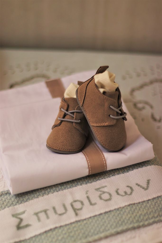 Cute brown leather baby shoes placed on embroidered cloth with Greek lettering.